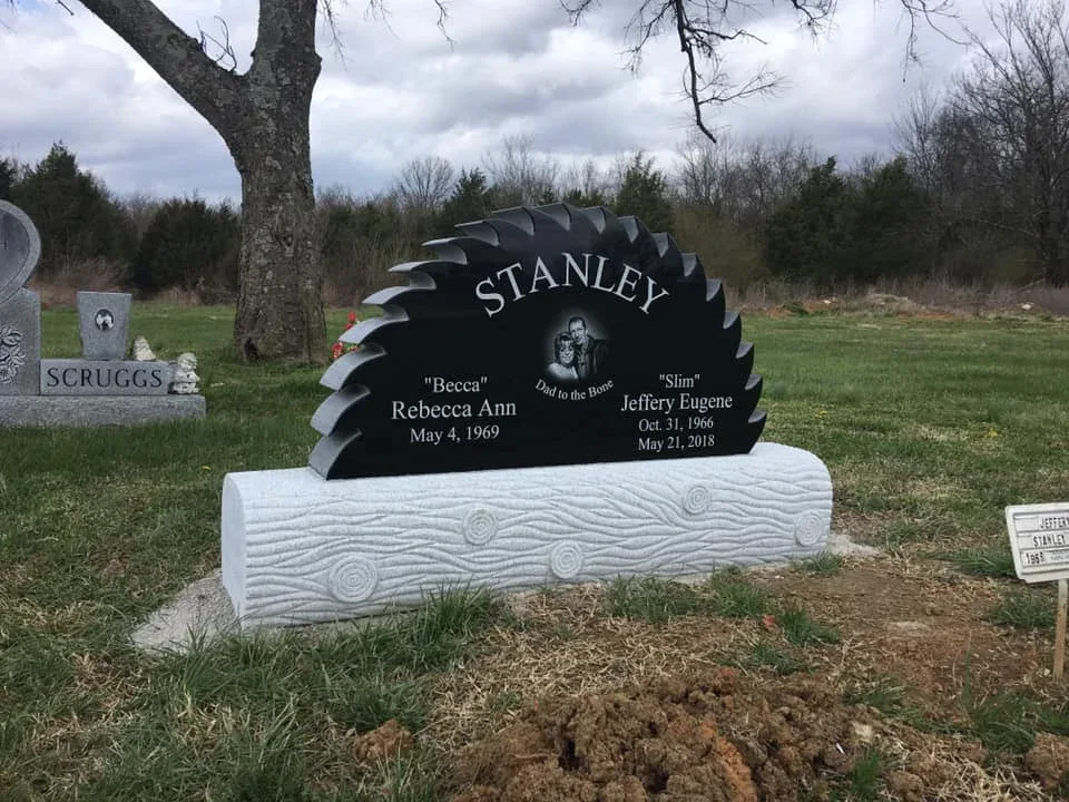 A black granite memorial shaped like a circular saw blade, standing on a base carved with a wood-grain pattern