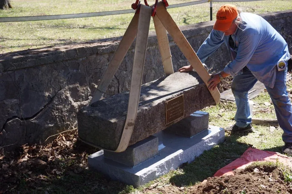 A craftsperson carefully positioning a substantial stone memorial using lifting equipment