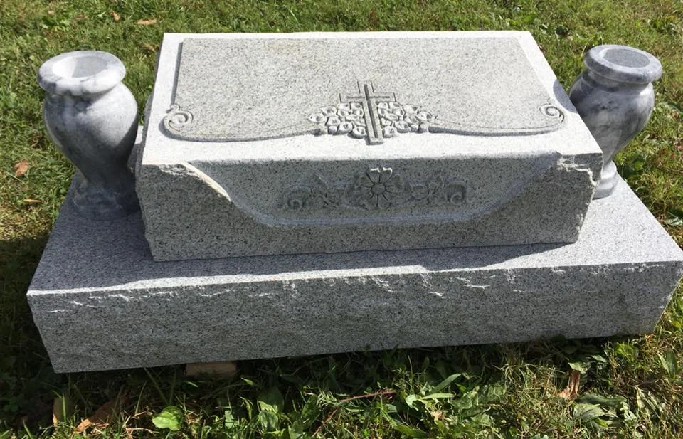 A low curved granite memorial with sculpted flowers, a cross and two vases
