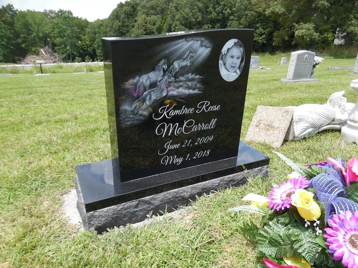 A black memorial with an engraved horse scene, a portrait and a personal inscription