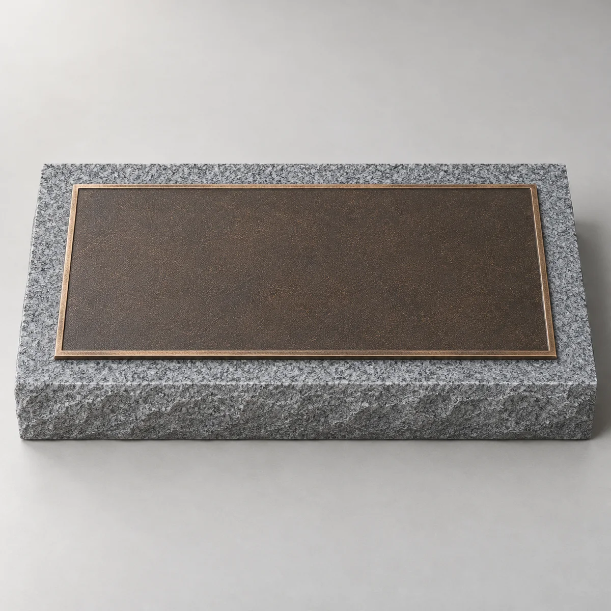 Blank dark bronze plaque with a raised metal border on a low grey granite backing