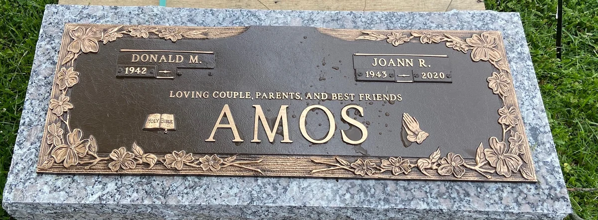 The Amos bronze companion marker on a granite surround, with raised lettering, flowers and a butterfly