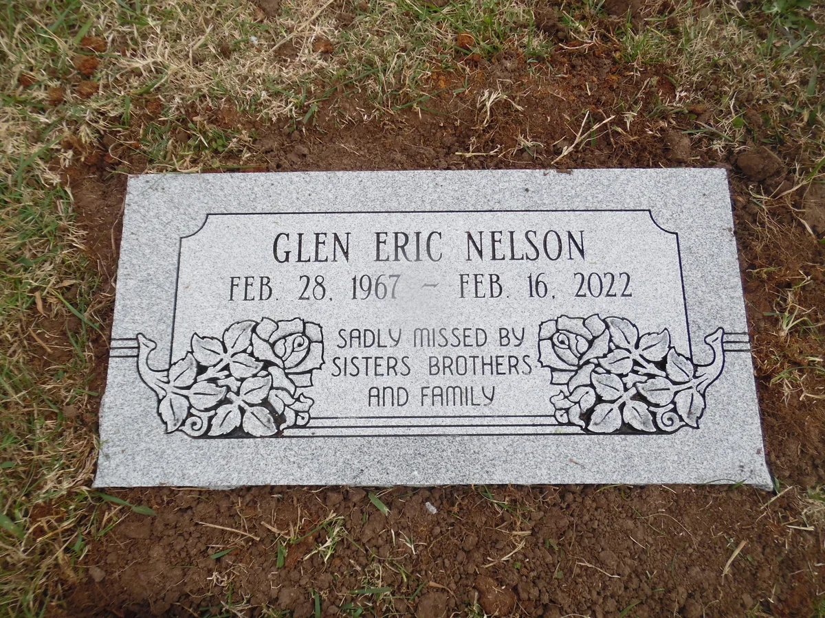 The Glen Eric Nelson flat grey marker with carved roses and a bordered inscription