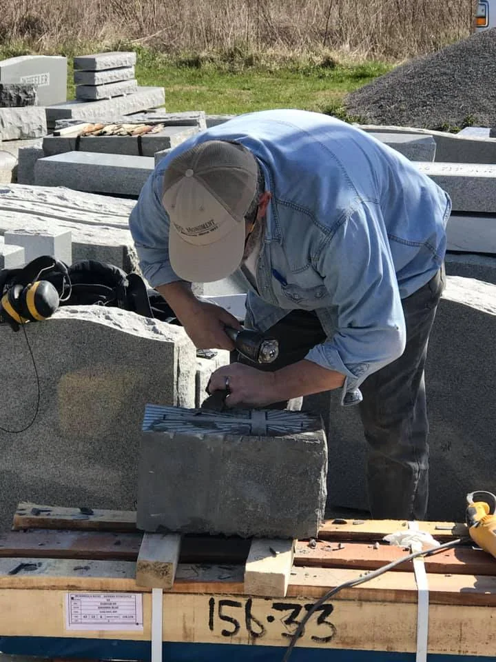 A person leaning over a piece of stone while working with a hand tool