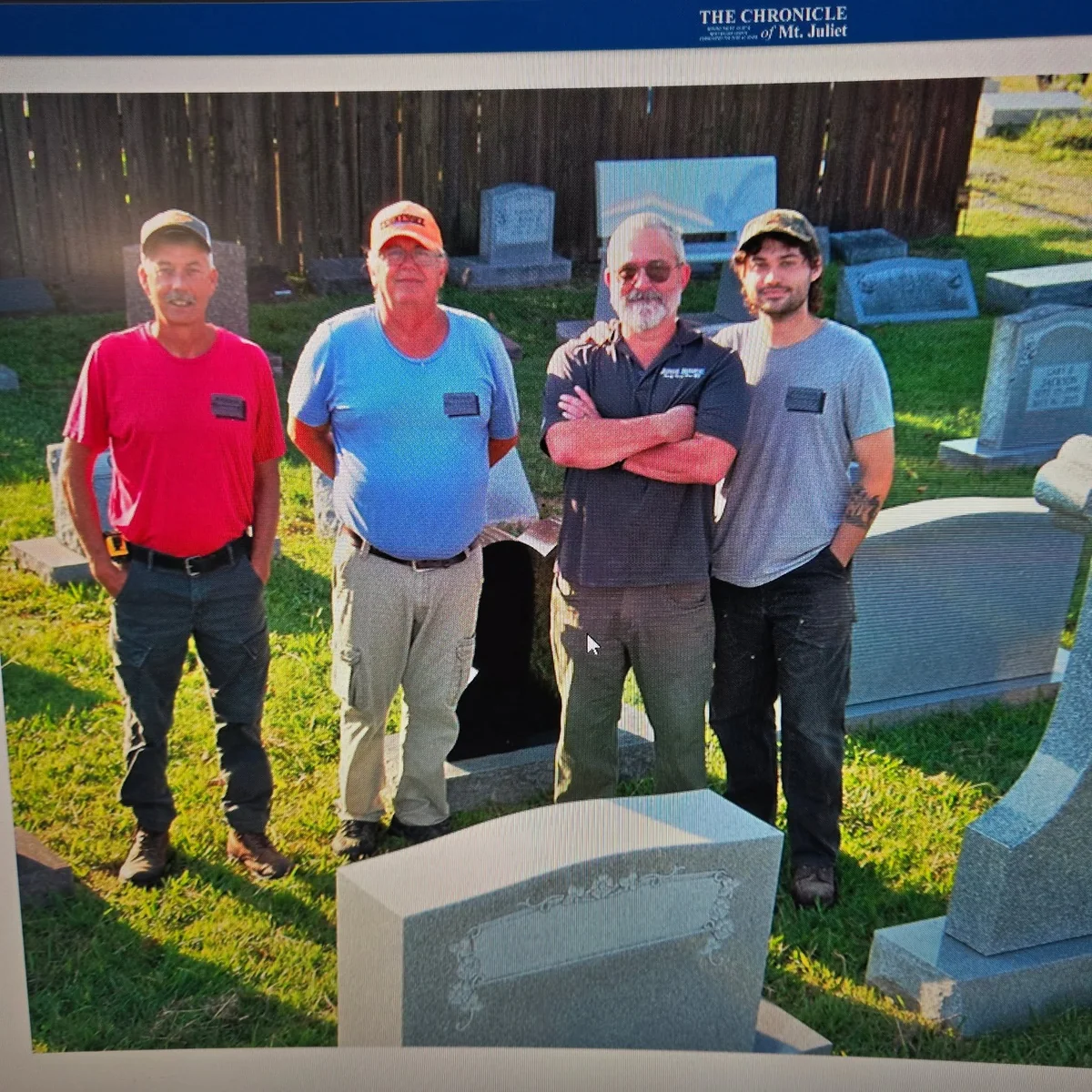 Archive newspaper photograph of four men standing together among memorials outdoors