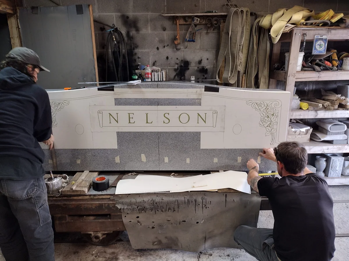 Two people preparing the lettering layout on a Nelson memorial in the workshop