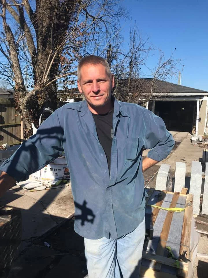 A man in a blue shirt beside a workbench outside the workshop