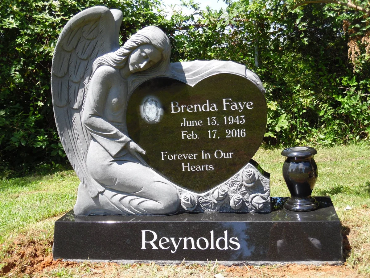 A carved angel rests against a polished heart on the Reynolds memorial, with roses at its base